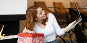 Eine junge Frau packt ein Weihnachtspäckchen aus und macht einen Videoanruf. Symbolbild: Getty Images / Jokic / iStock / Getty Images Plus