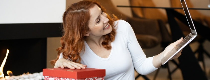 Eine junge Frau packt ein Weihnachtspäckchen aus und macht einen Videoanruf. Symbolbild: Getty Images / Jokic / iStock / Getty Images Plus