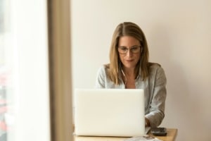Eine Frau sitzt an einem Tisch. Sie trägt Kopfhörer und tippt etwas in ihren Laptop.