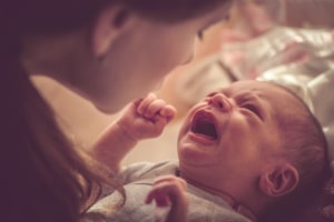 Mutter beugt sich über ein Schreibaby.