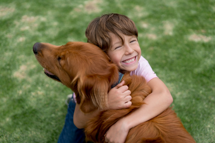 Ein Junge umarmt seinen Hund und lächelt.