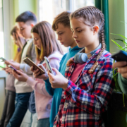Brauchen wir ein Social-Media-Verbot? Kinder stehen in der Schule mit dem Smartphone in der Hand.