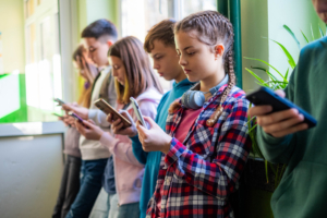 Kinder stehen in der Schule mit dem Smartphone in der Hand.