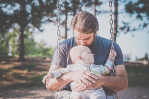 Ein einsamer Papa sitzt mit seinem Baby auf einer Schaukel.