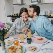 Glückliches Paar Ein Mann küsst seine Frau am Frühstückstisch. Beide sehen glücklich aus.