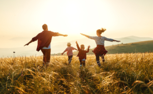 Eine Glückliche Familie läuft in der Abendsonne über eine Wiese.