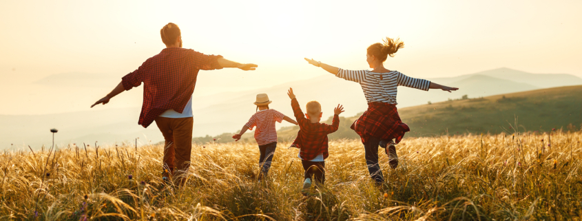 Eine Glückliche Familie läuft in der Abendsonne über eine Wiese.