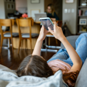 Teenager liegt zuhause auf dem Sofa und scrollt durch ihr Handy.